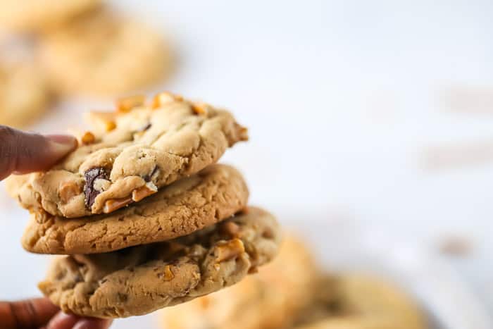 Three Butterscotch Pretzel Cookies being held in a hand with cookies in the background.