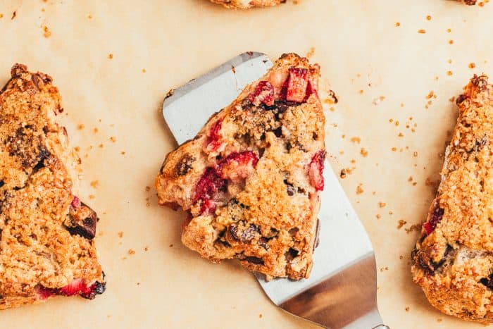 A chocolate strawberry scones on a spatula with a few other scones. 