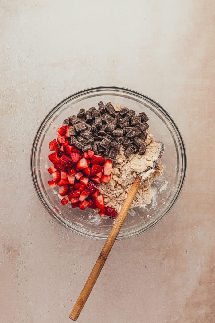 A glass bowl with the dry ingredients and chopped strawberries and chocolate.