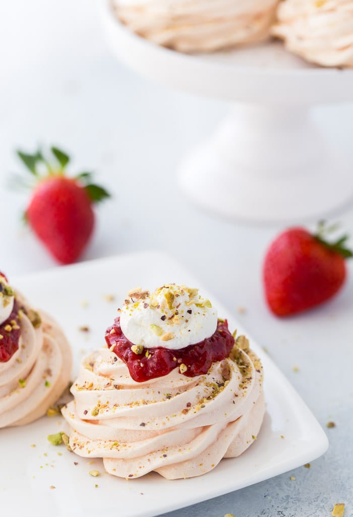 Delicate rosewater pavlova with pistachios is topped with strawberry compote and whipped cream for an elegant dessert.