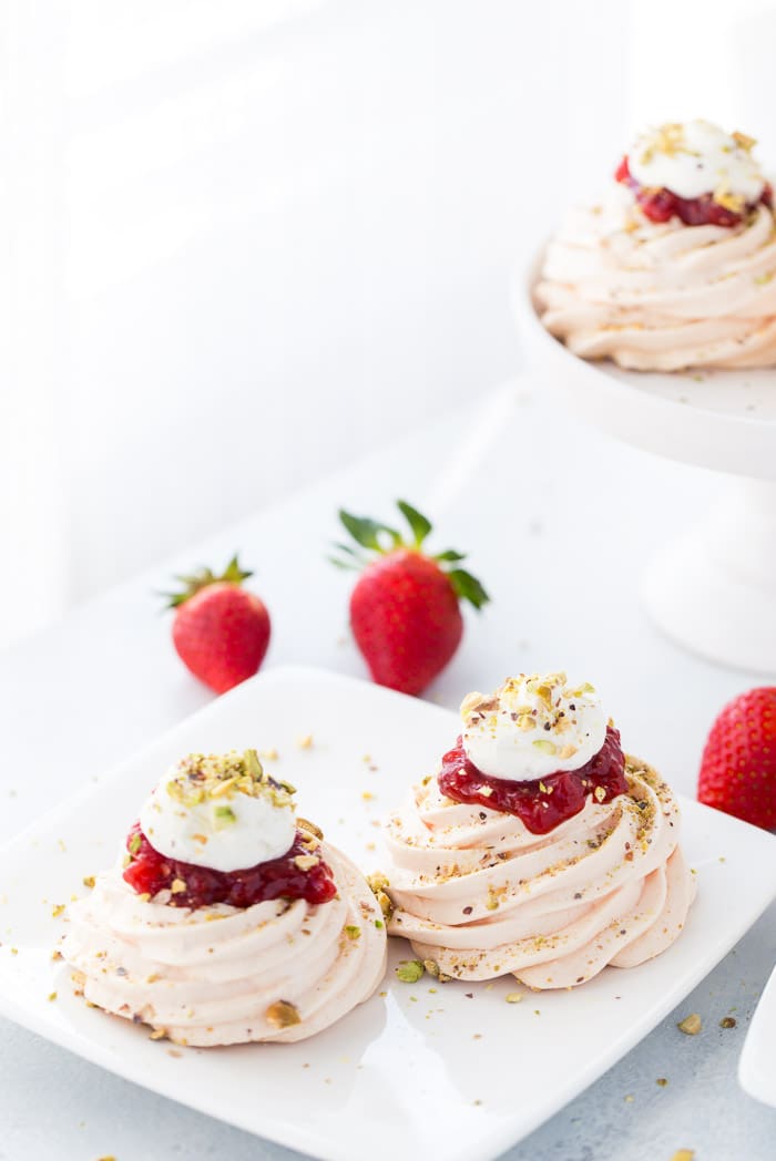 Delicate rosewater pavlova with pistachios is topped with strawberry compote and whipped cream for an elegant dessert.