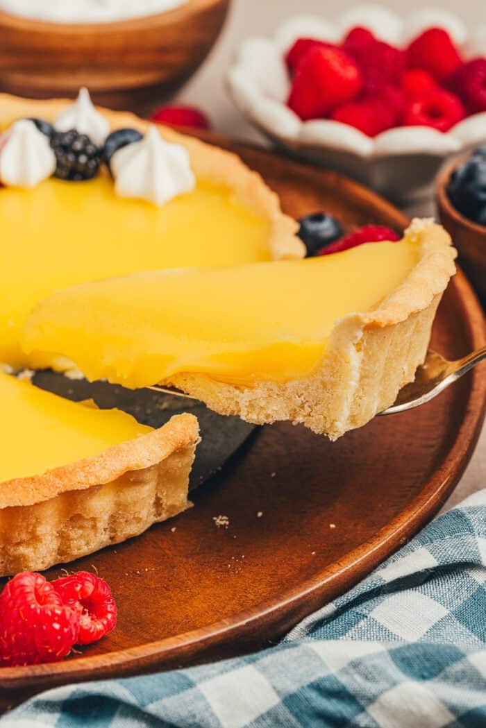 A slice of homemade lemon tart is being removed from the tart.