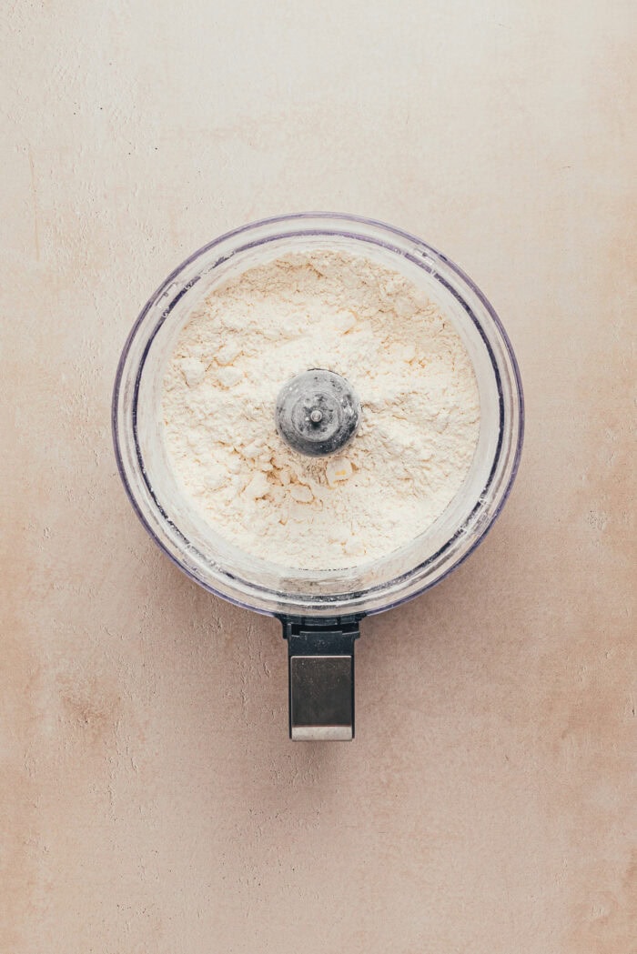 A food processor with the ingredients used to make a shortbread tart crust.