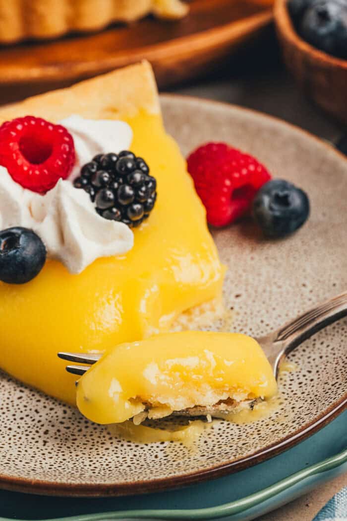 A plate with a slice of homemade lemon tart on it with a fork taking a bite.