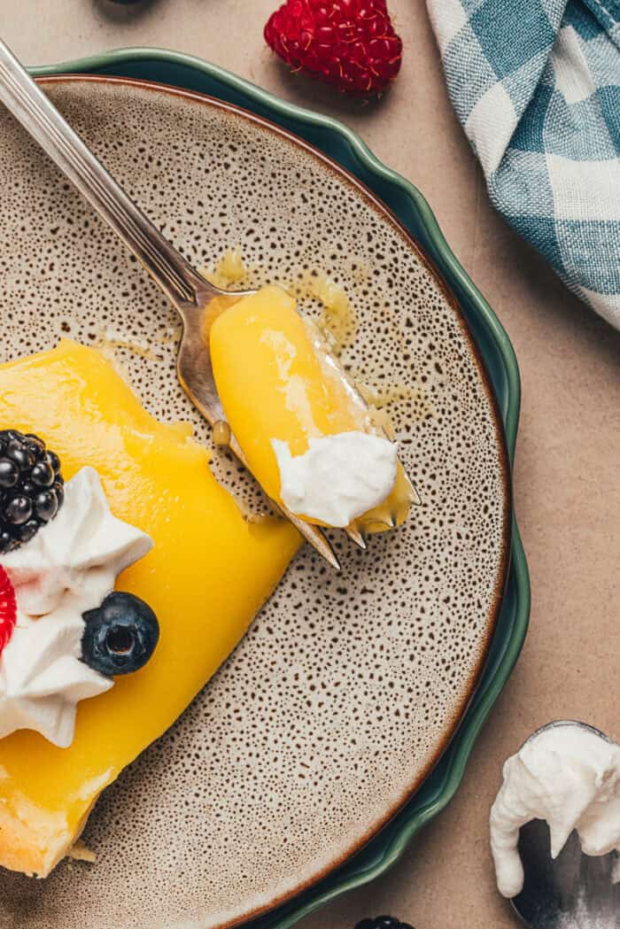 A plate with a slice of homemade lemon tart on it with a fork taking a bite.