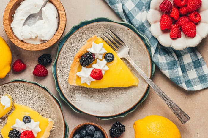 A few plates with slices of classic lemon tart on them, decorated with berries and whipped cream.