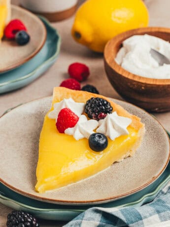 A slice of classic lemon tart on two plates, decorated with berries and whipped cream.
