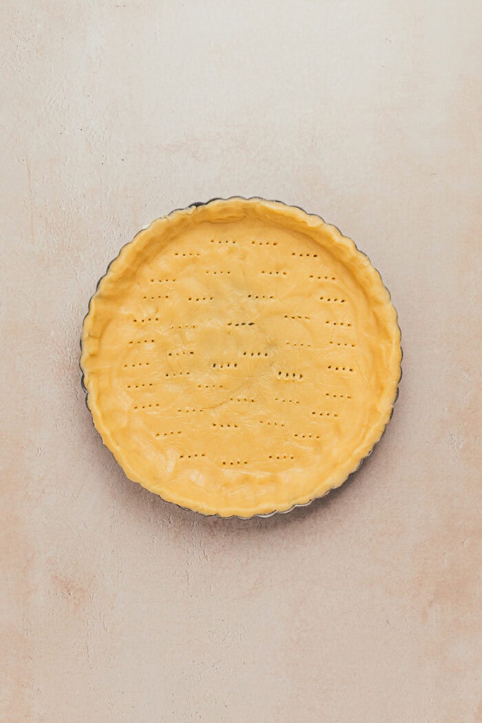 An unbaked shortbread tart crust with wholes poked into it in a tart pan.