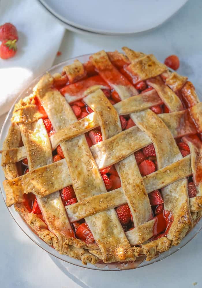 A freshly baked strawberry pie with juices overflowing and fresh strawberries on the table. 