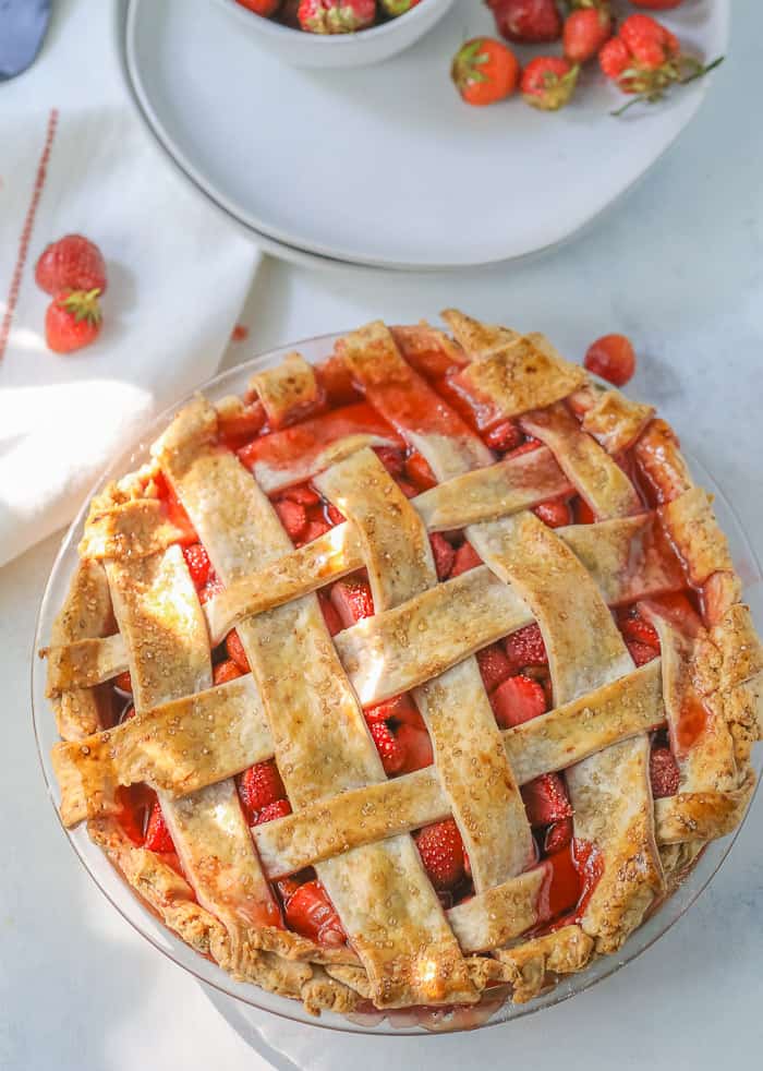 A picture of a homemade strawberry pie on a table with a bowl of fresh strawberries. 
