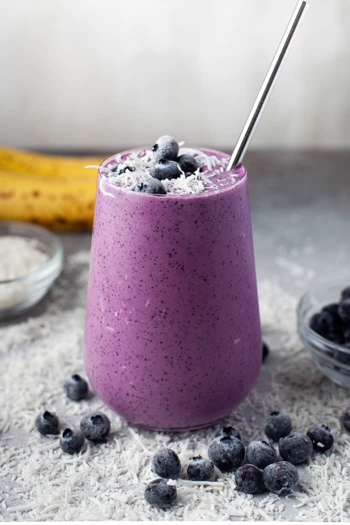 Healthy Blueberry Smoothie in a glass with blueberries and coconut flakes around it. 