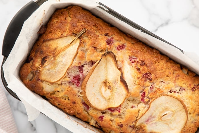 Pear and Raspberry Bread in a loaf pan on a marble background. 