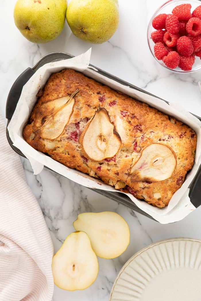 Pear and Raspberry Bread with a marble background and a few cut pears and raspberries around it.