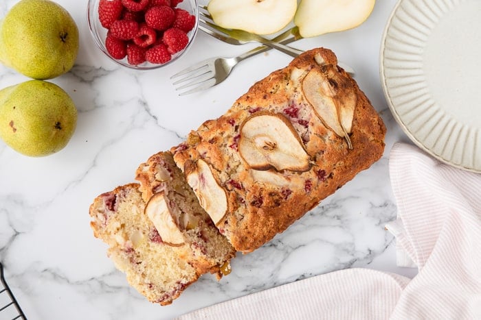 Pear and Raspberry Bread sliced on a marble background with pears and raspberries. 