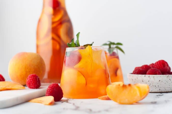 A glass and pitcher of peach rose sangria.