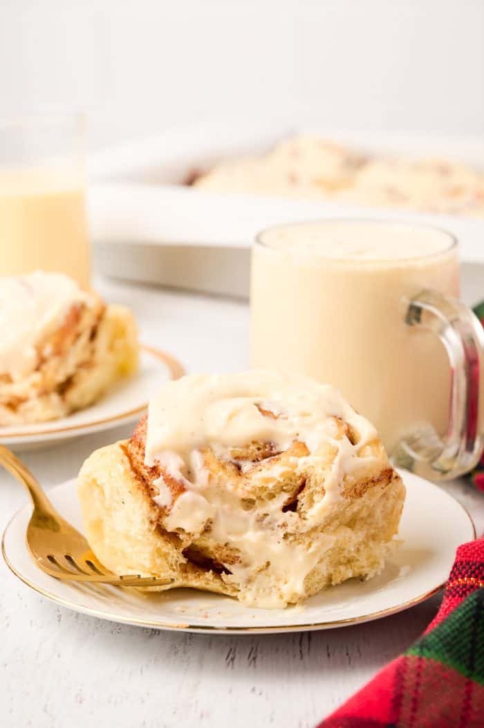 Eggnog cinnamon roll on a plate with a bite out of it.