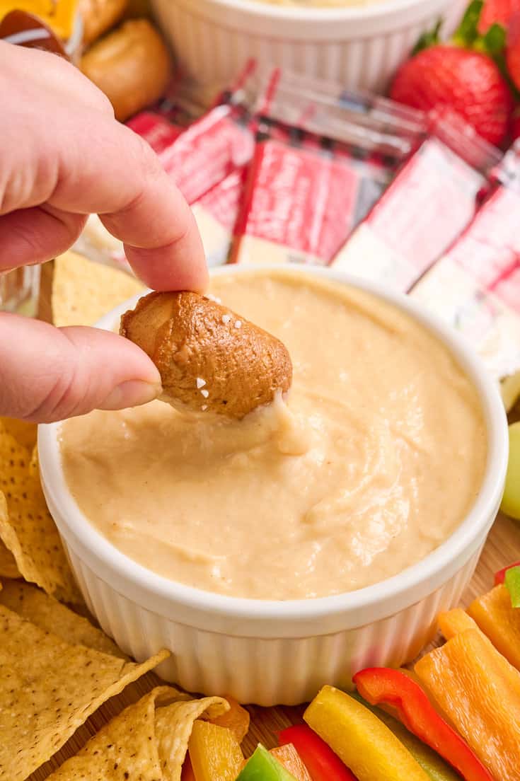 A hand dipping a pretzel into beer cheddar cheese dip. 