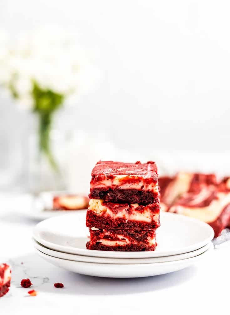 A stack of red velvet cheesecake brownies on white plates.
