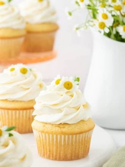 Chamomile cupcakes in front of a vase.