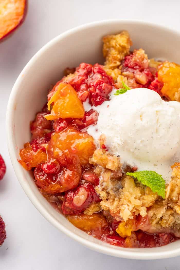 Peach raspberry crumble in a bowl with vanilla ice cream.