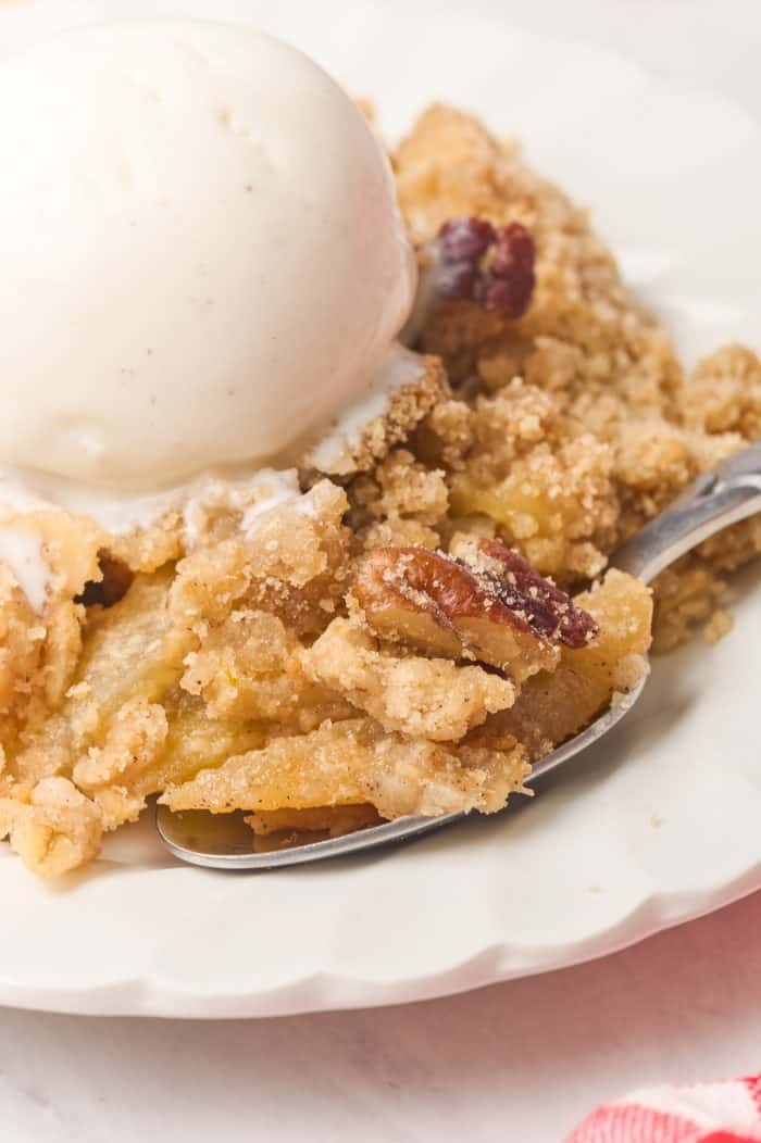A plate of apple crisp with a scoop of ice cream with a spoon.