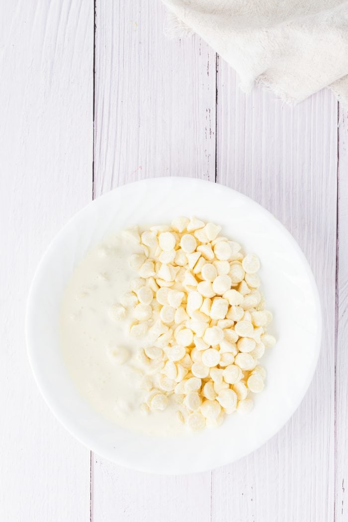 White chocolate chips mixed with heavy cream in a white bowl.