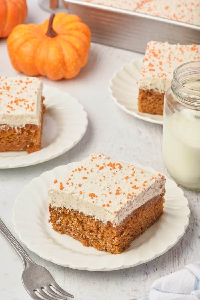 Three white plates with pumpkin cake bars and a glass of milk.