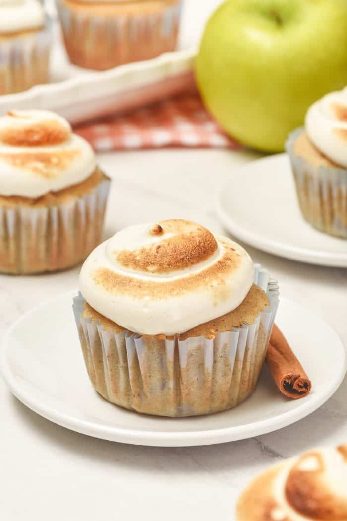 Two spiced apple cupcakes on white plates with a cinnamon stick.