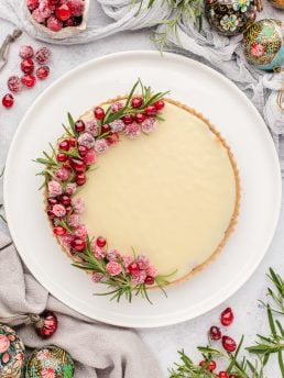 An overhead picture of the white chocolate cranberry tart with rosemary and cranberries around it as decorations.