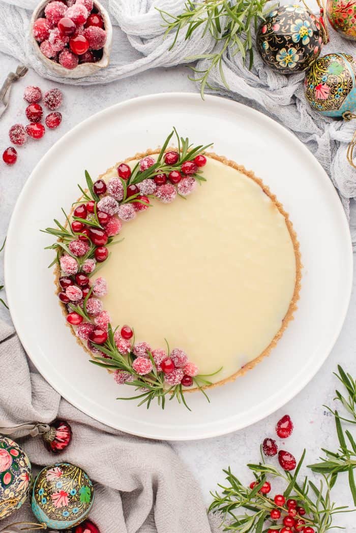 An overhead picture of the white chocolate cranberry tart with rosemary and cranberries around it as decorations.