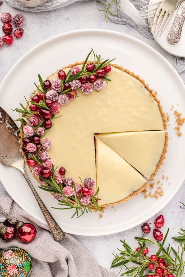 An overhead image of a white chocolate cranberry tart on a white plate with slices made into it.