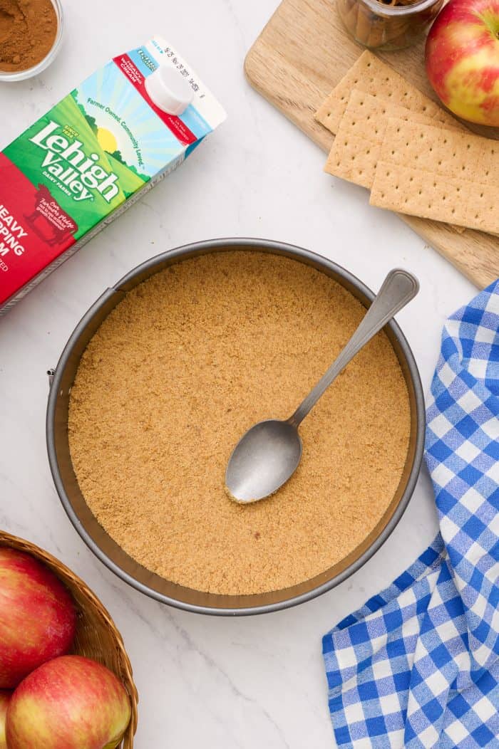 A cheesecake pan with the graham cracker crumbs pressed into it with a spoon. 