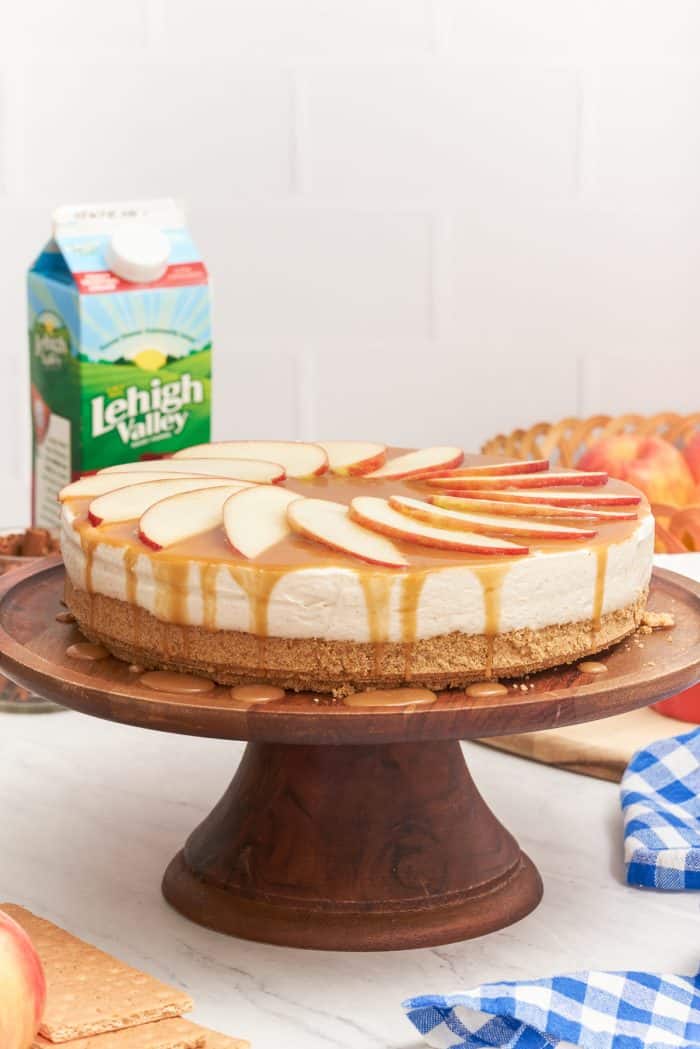 A no bake caramel apple cheesecake on a wooden cake stand.