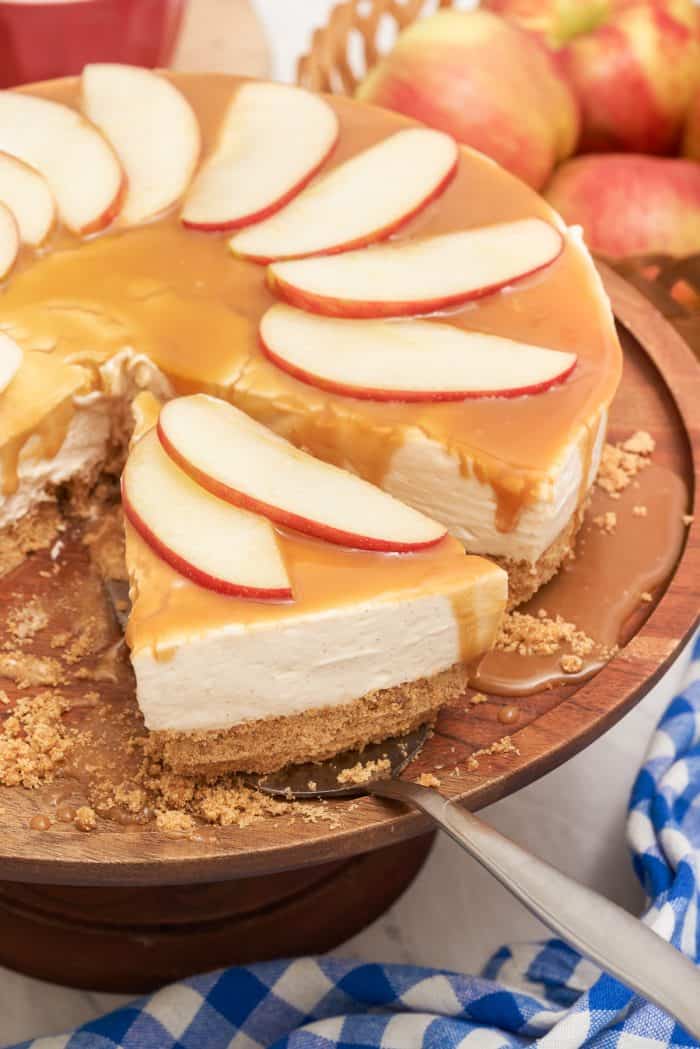 A slice of apple caramel cheesecake being removed from the whole cheesecake.