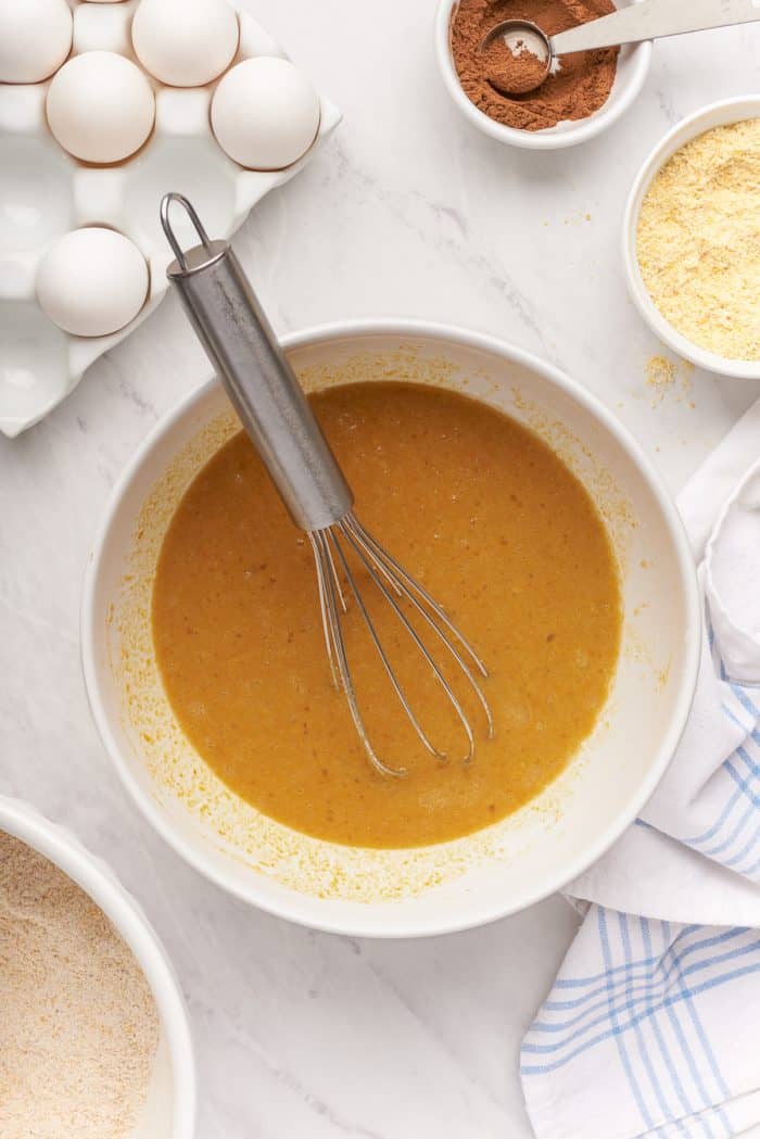 A white bowl with the pumpkin puree mixed with eggs and a whisk.