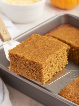 A slice of pumpkin cornbread being lifted from the baking pan.