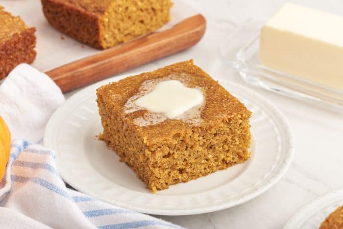 A slice of pumpkin cornbread with melted butter on a white plate.