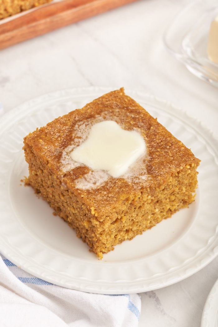 A plate with a slice of pumpkin cornbread with melted butter.