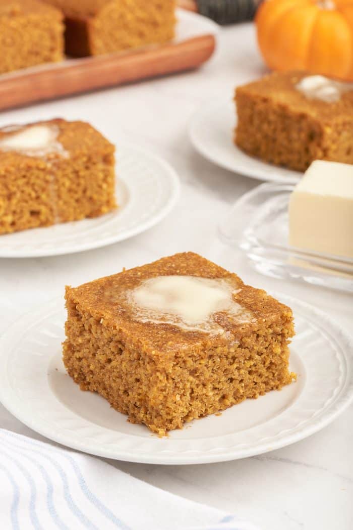 Three plates with slices of pumpkin cornbread that has melted butter on it.