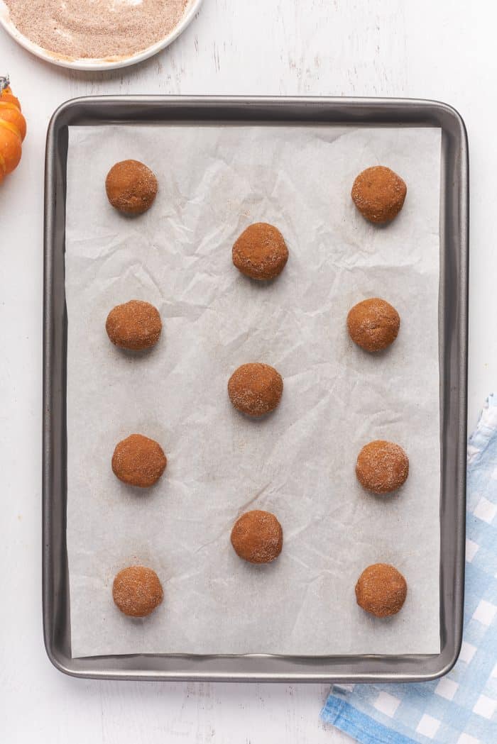 A baking sheet with parchment paper with balls of raw cookie dough.