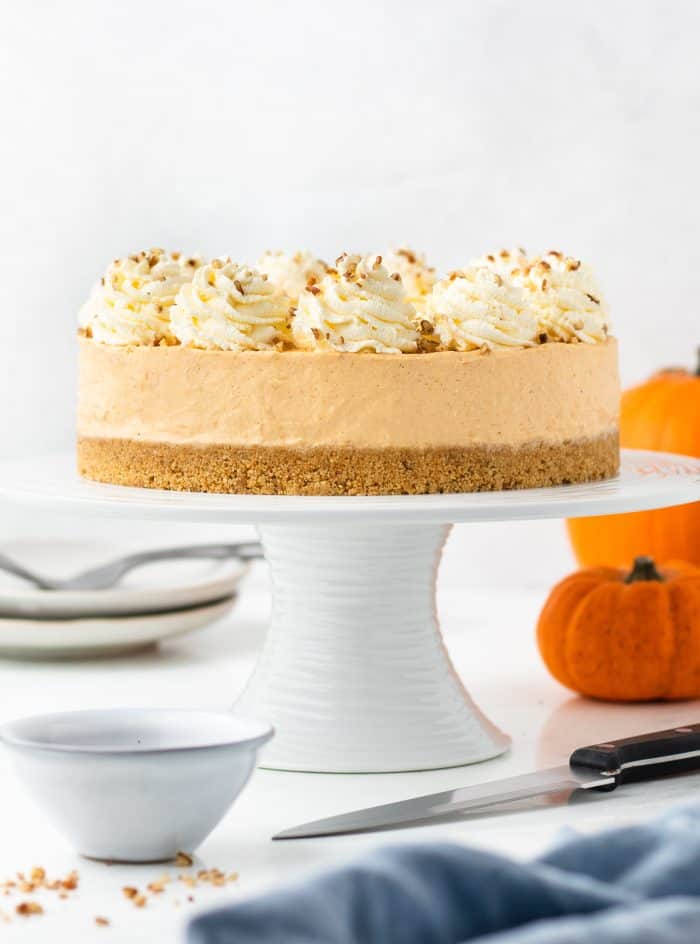 A no bake pumpkin cheesecake on a white cake stand with fall decorations.