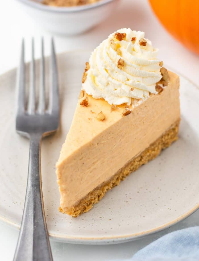 A slice of pumpkin cheesecake on a plate with pumpkins in the background.