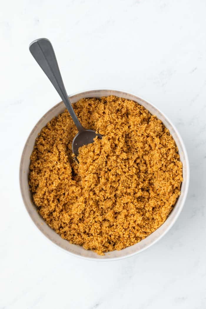 The graham cracker crumbs mixed with melted butter in a bowl with a spoon.