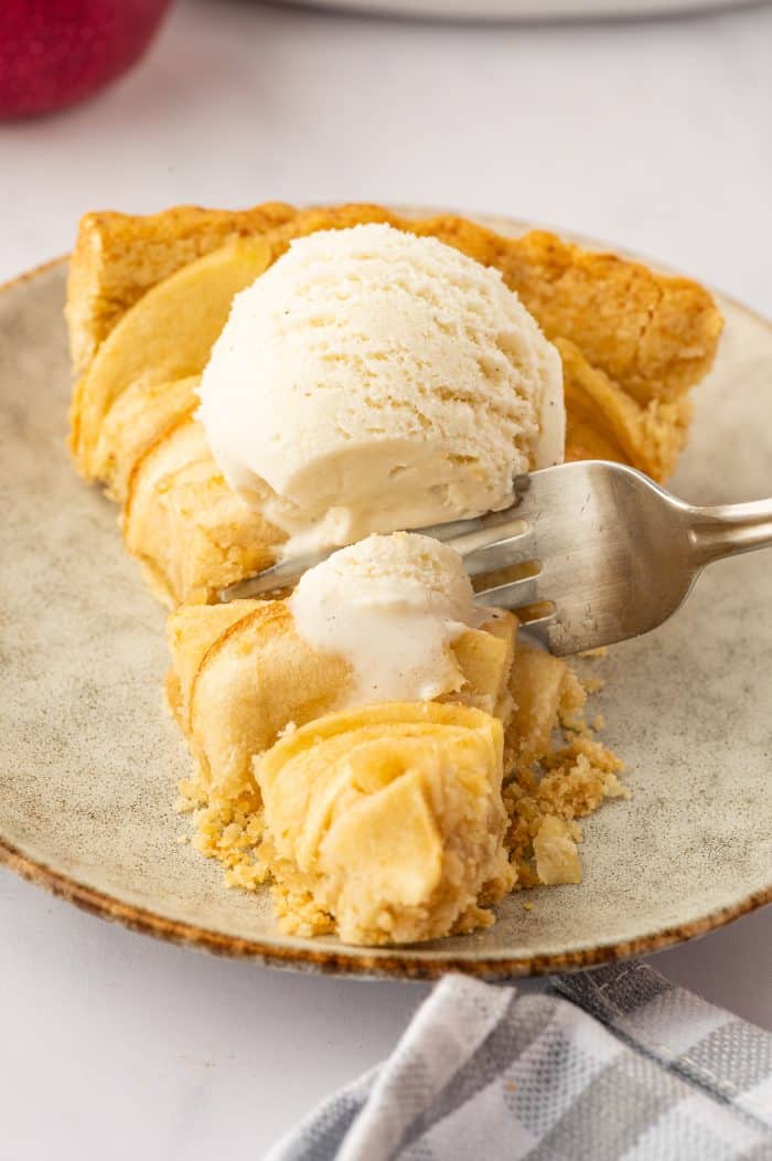 A slice of apple tart with a scoop of vanilla ice cream and a fork cutting into it.