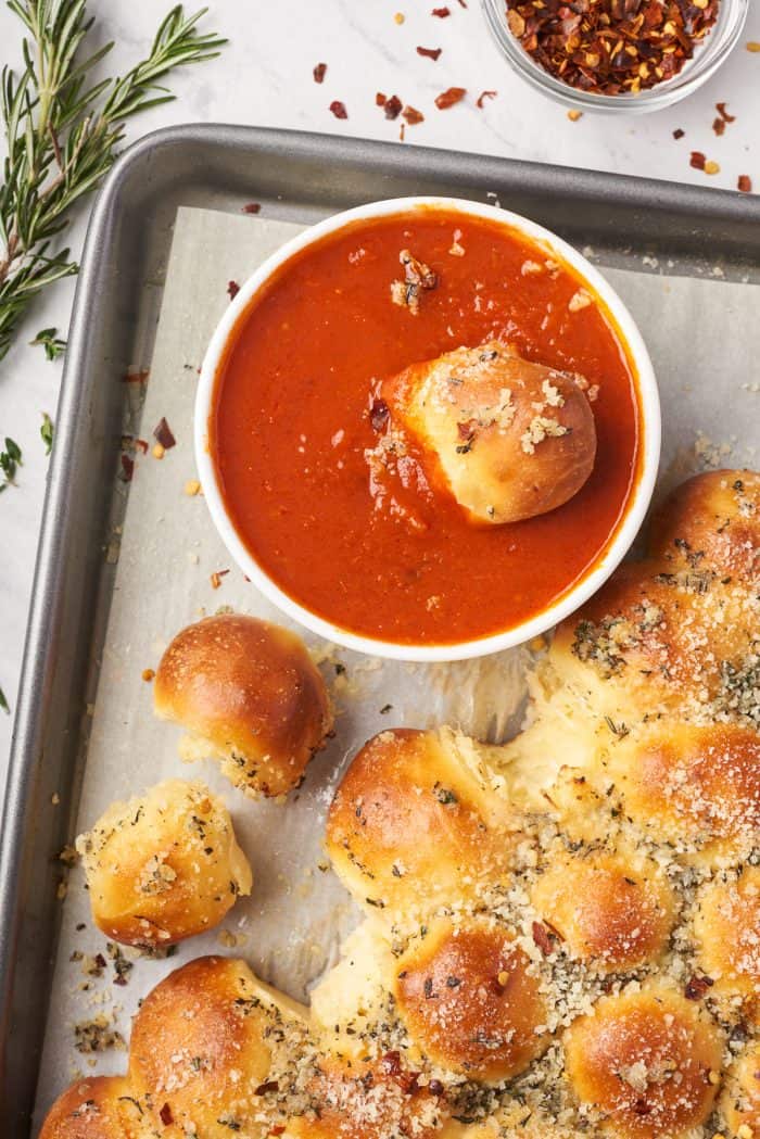 A piece of the pull apart bread dipped into a bowl of marinara sauce.