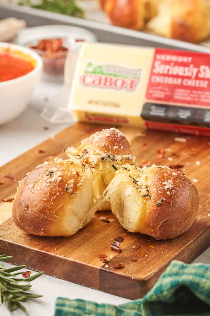 Three bread dough balls on a wooden cutting board with a block of cheese in the background.