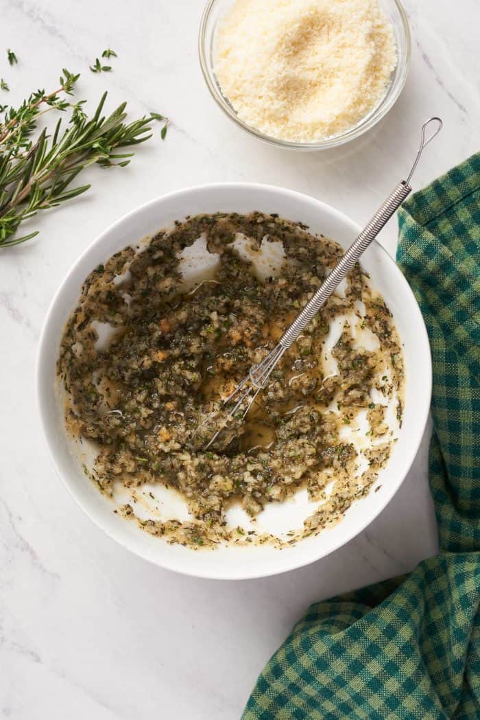 A white bowl with the herbs and melted butter mixed together.