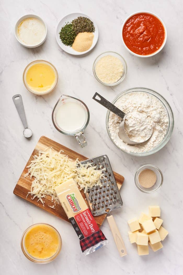 An image of the ingredients for a Christmas tree pull apart bread with shredded cheese on a wooden cutting board.
