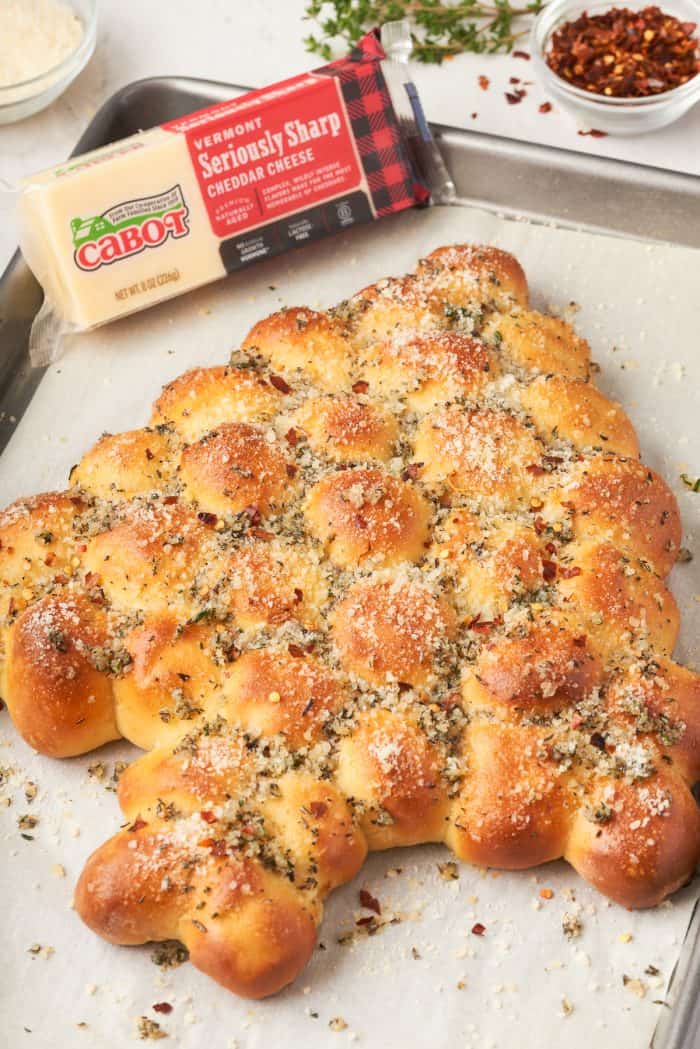 An image of a Christmas tree bread that is pull apart on a baking sheet with a block of cheese.