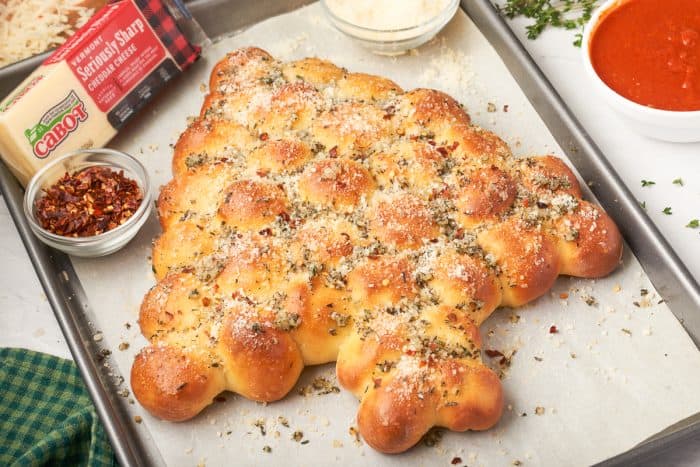 An image of a Christmas tree bread that is pull apart on a baking sheet with a block of cheese.